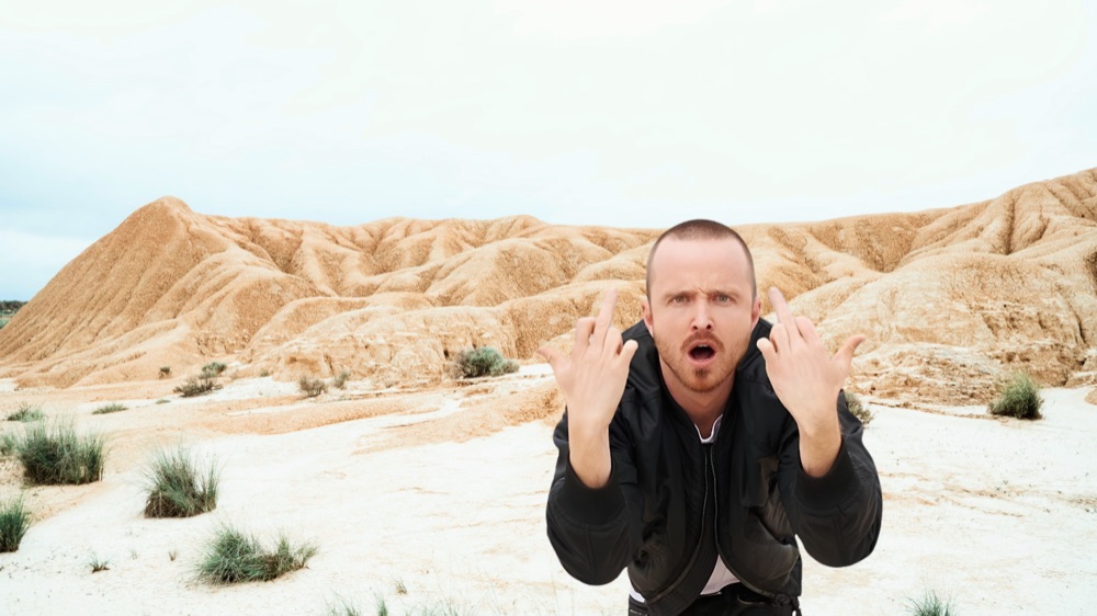 Hombre con chaqueta negra gesticulando ante las colinas del desierto